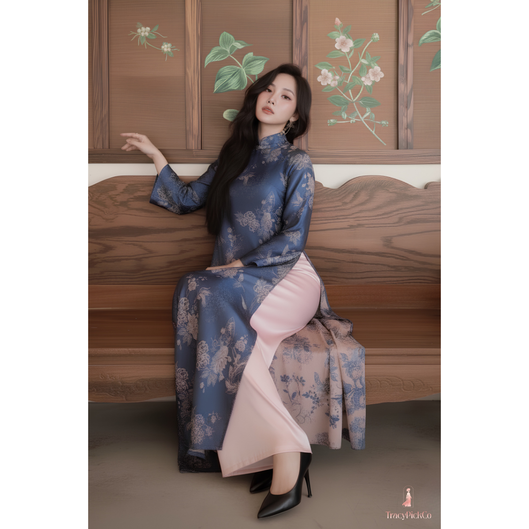 A woman wearing a blue floral vietnamese dress with a pink inner skirt sits on a wooden bench in front of a wooden wall with floral paintings.